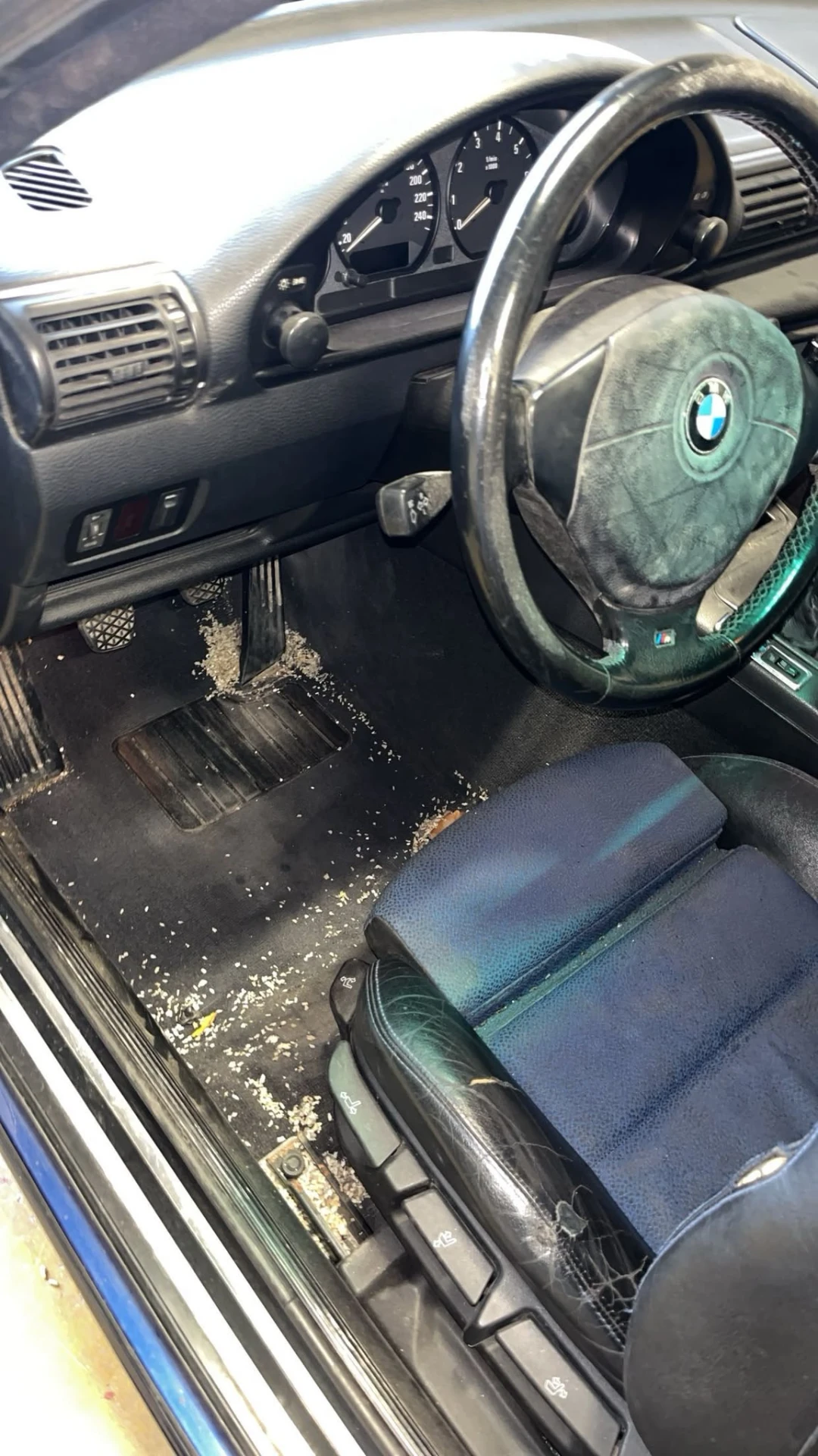 Habitacle BMW E30 avant intervention — tapis couverts de débris et sièges sales